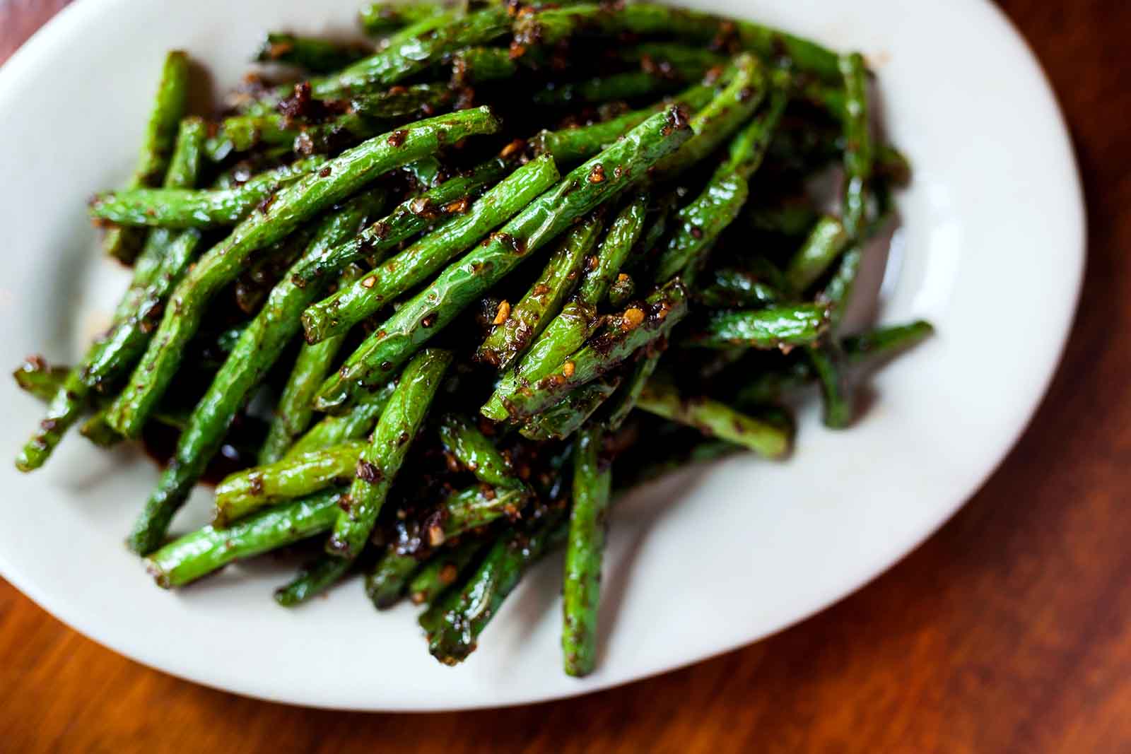 A plate of sautéed green beans with seasoning, served on a wooden table.