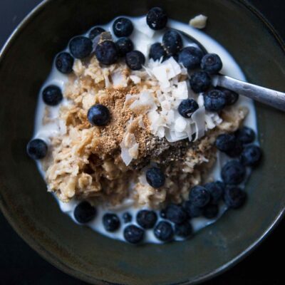 A bowl of yogurt topped with granola, fresh blueberries, and coconut flakes, served with a spoon, on a dark background.